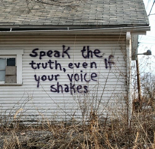 An abandoned building with "Speak the truth, even if your voice shakes" spray painted on the side.