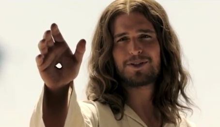 a man with a beard and longer hair wearing a white tunic extends his hand with a hole in the palm toward the viewer