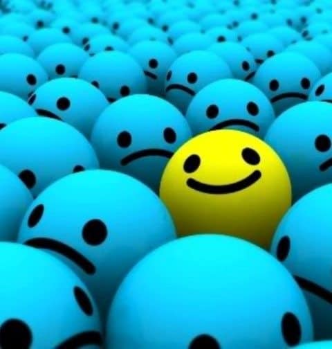 Yellow smiley happy face ball among blue sad face balls.