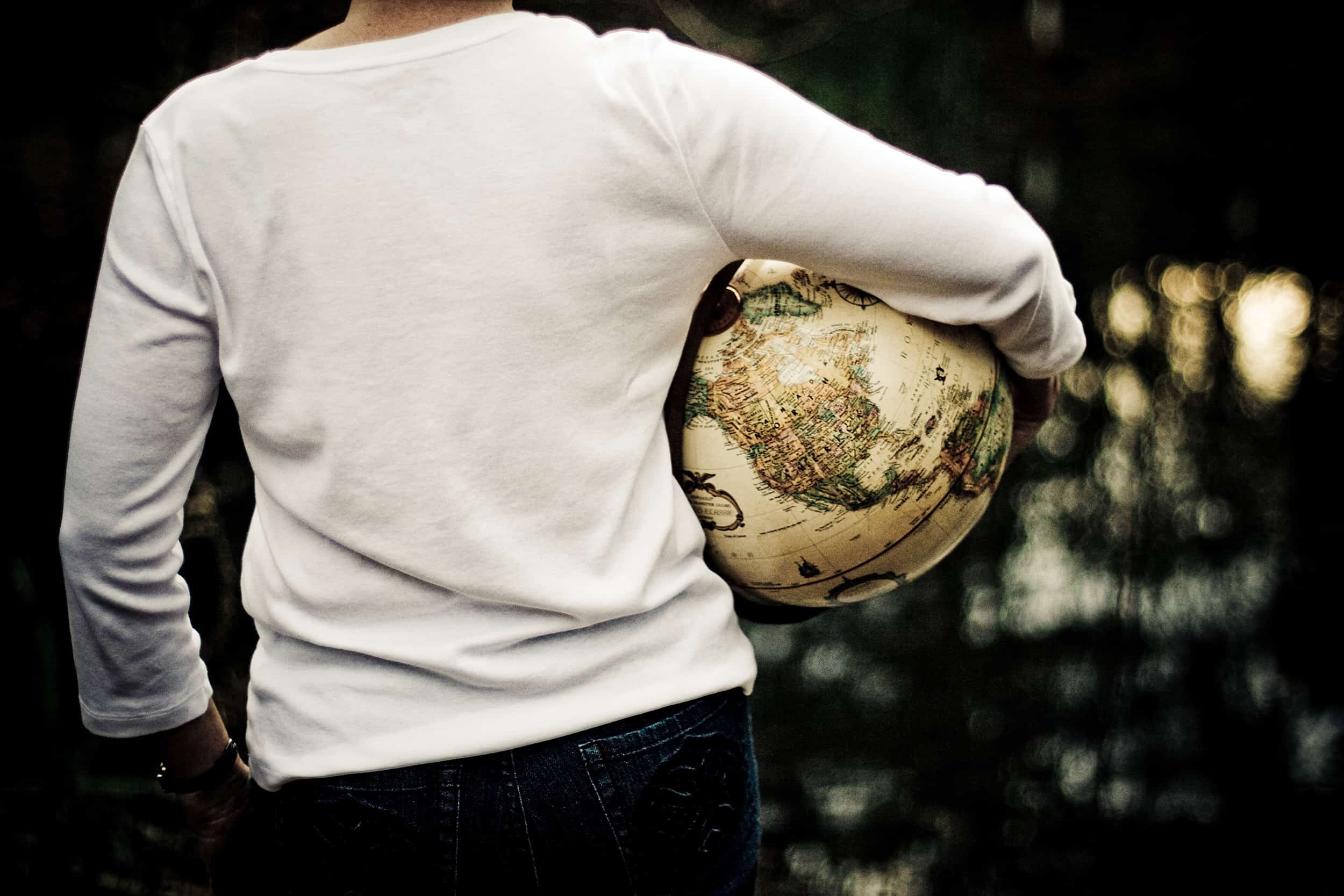 The torso of a person is seen from the back and they are holding a globe under an arm.