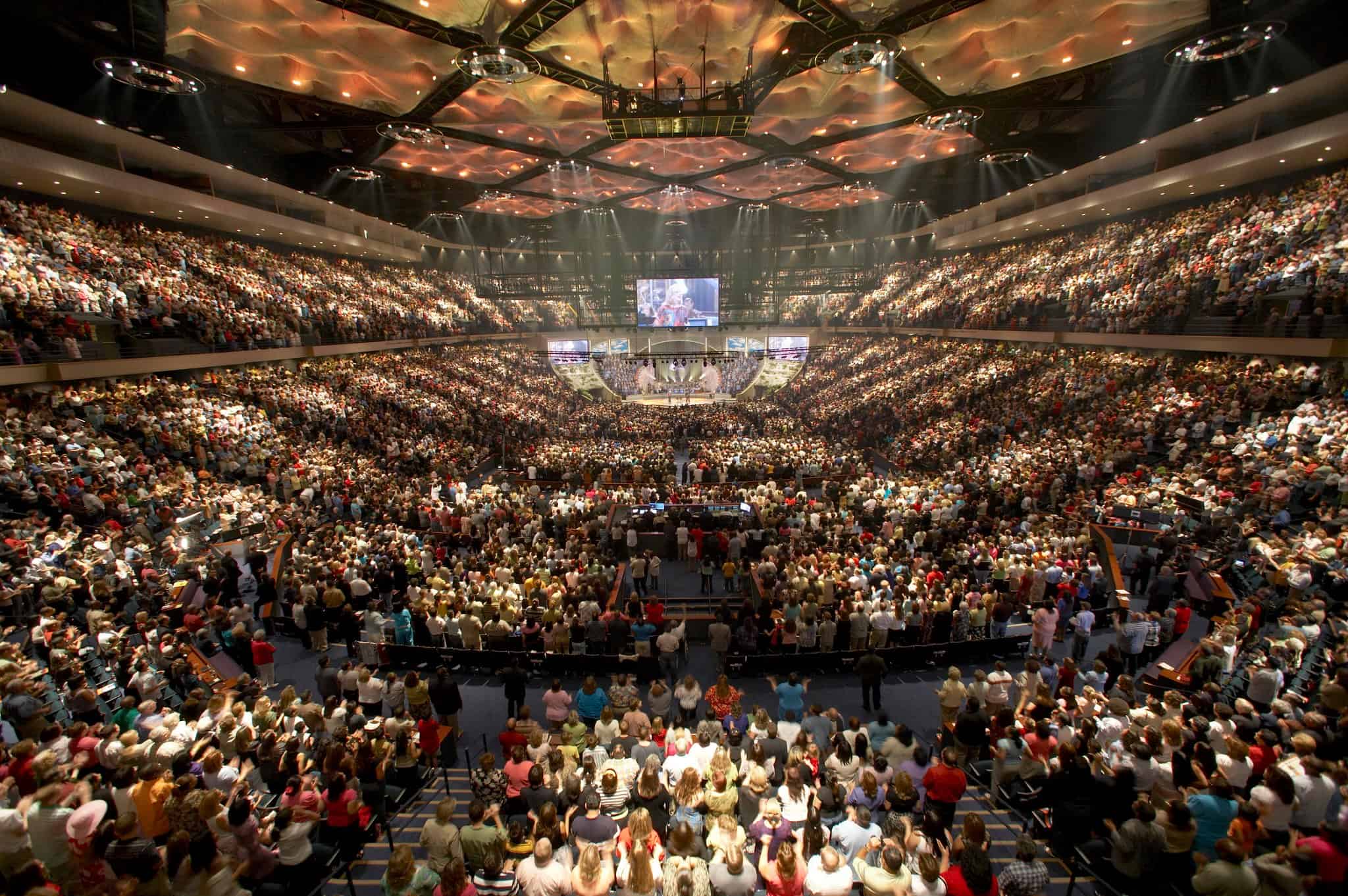 The stadium-like interior of a mega church is shown filled with people.