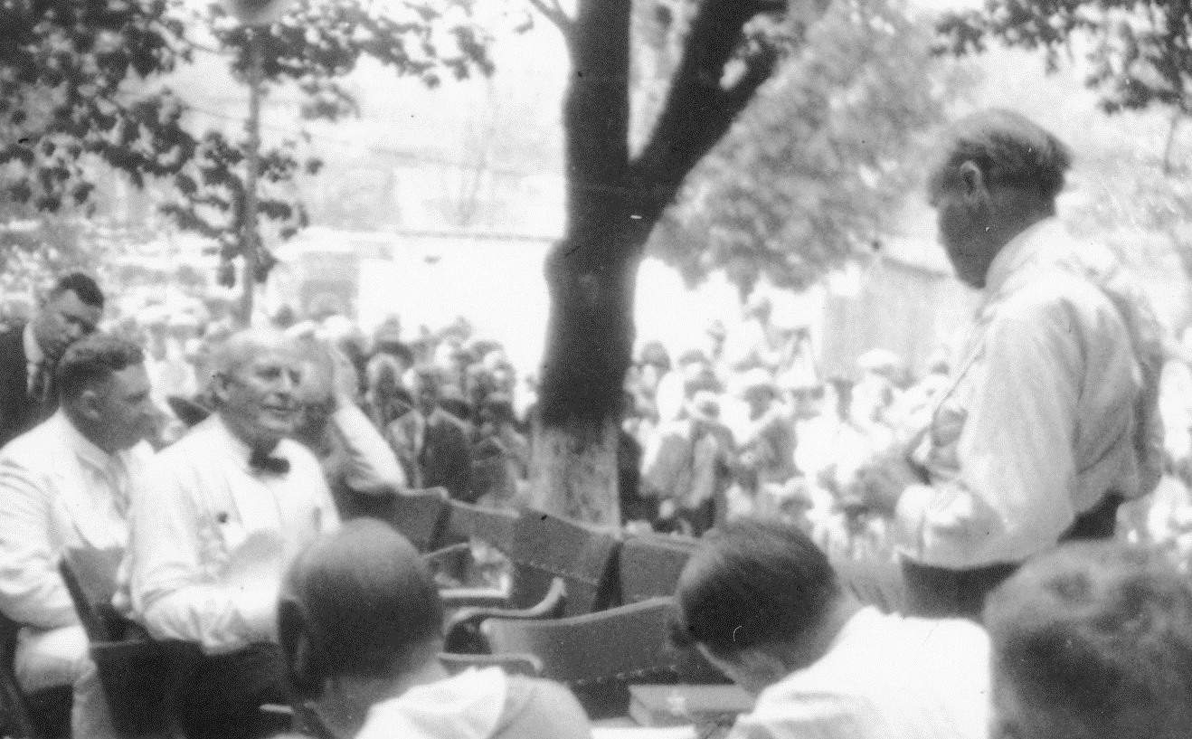 The black and white image shows the outdoor proceedings of the Scopes trial with multiple men dressed in white dress shirts.