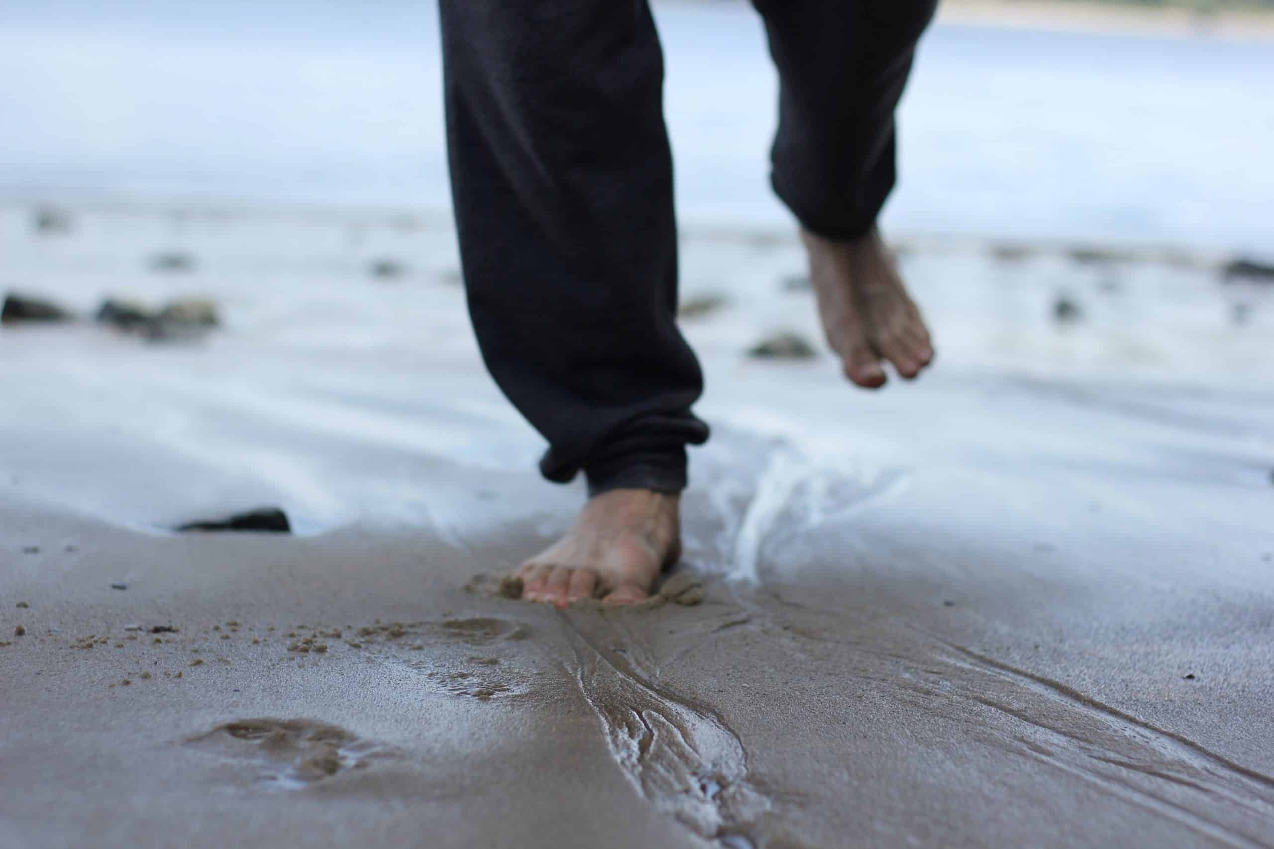 A man's feet are seen close up running through sand at the beach.