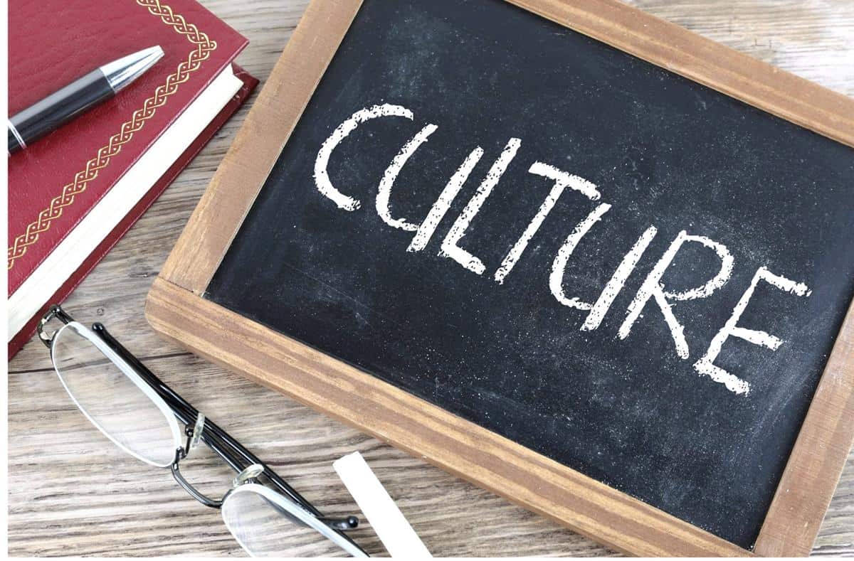 The word "culture" is written on a small wood framed chalk board with a pair of glasses in the foreground and a red notebook with a black pen set on top off to the left.