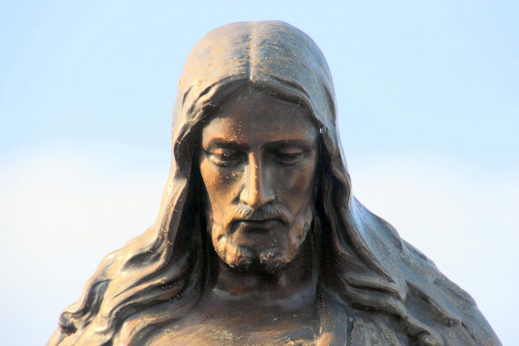An old statue depicting a version of Jesus is shown with his eyes downcast.