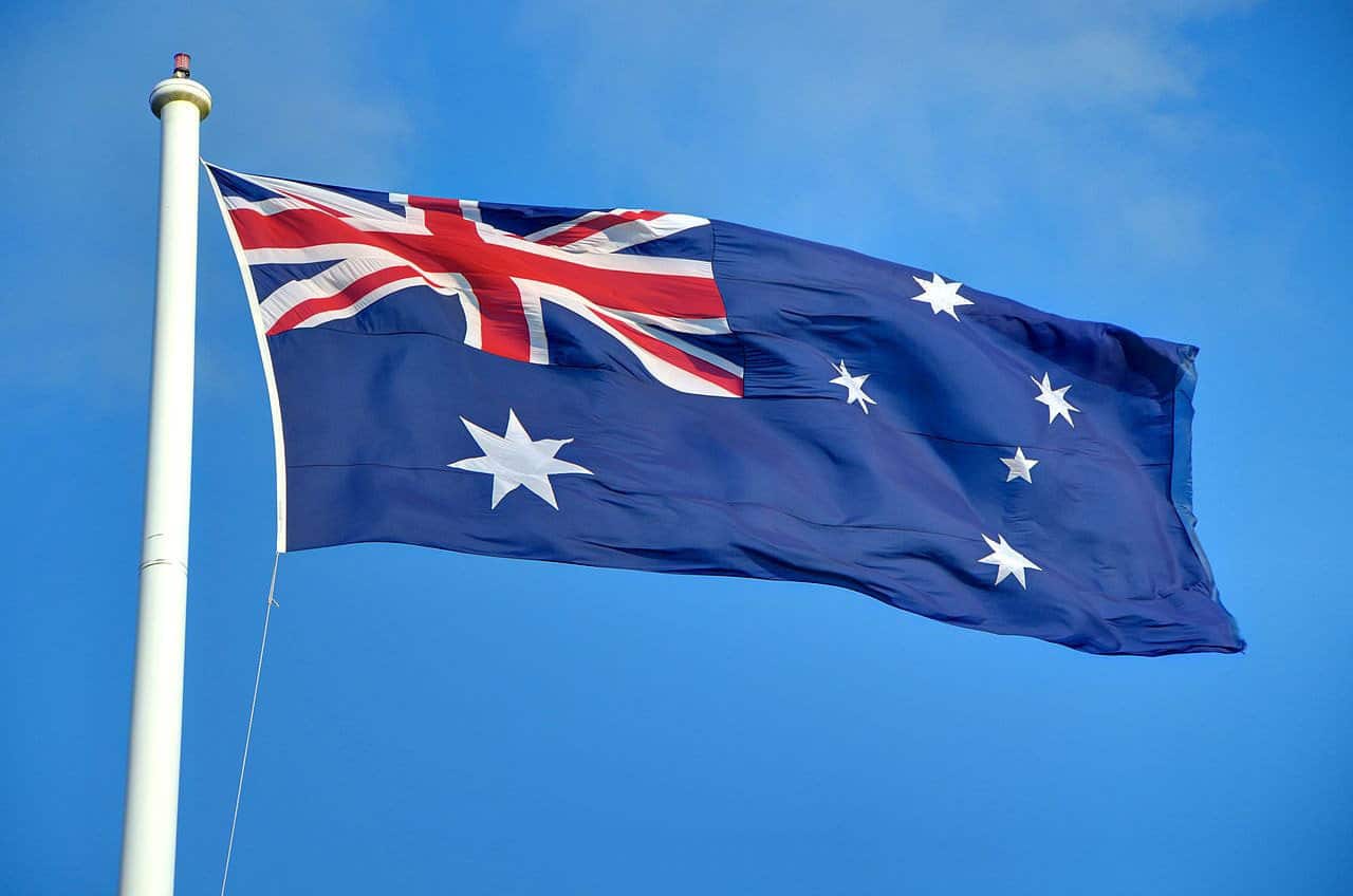An Australian flag is shown waving in the wind against a blue sky.