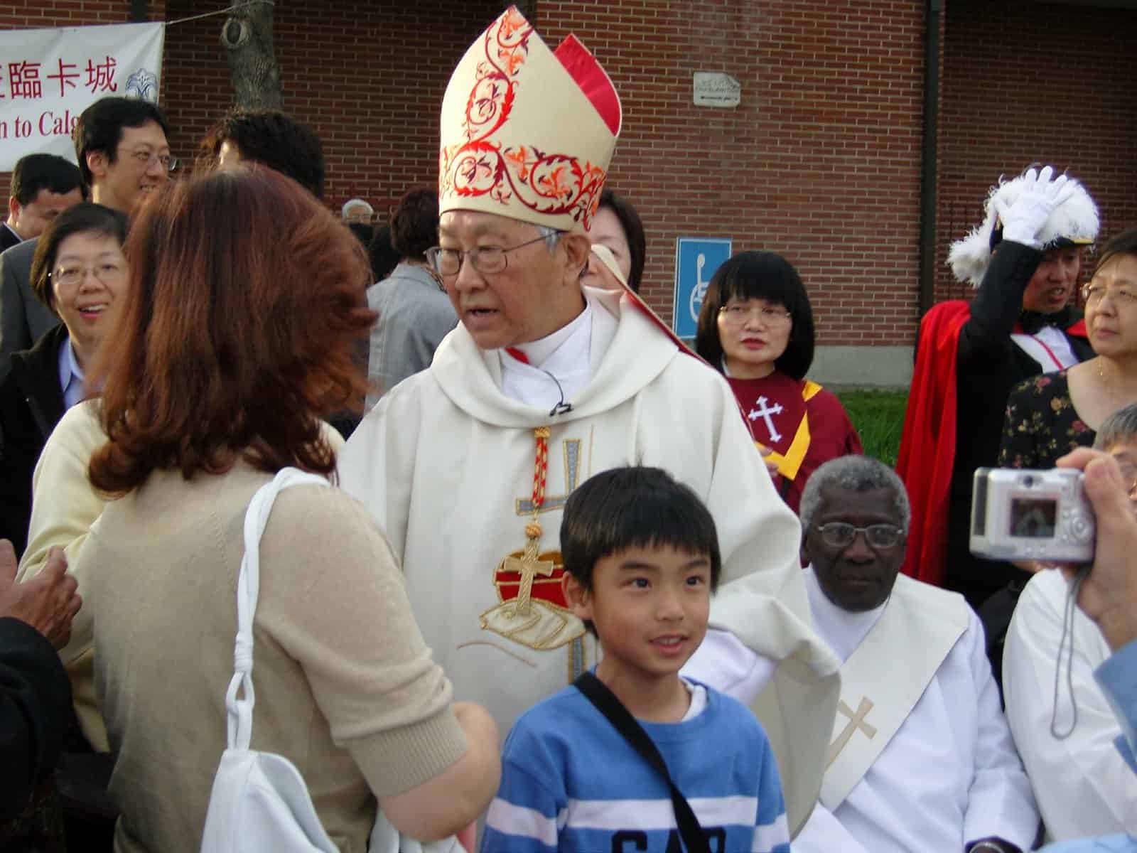 A Catholic cardinal of seemingly Asian decent stands in a crowd speaking to a woman