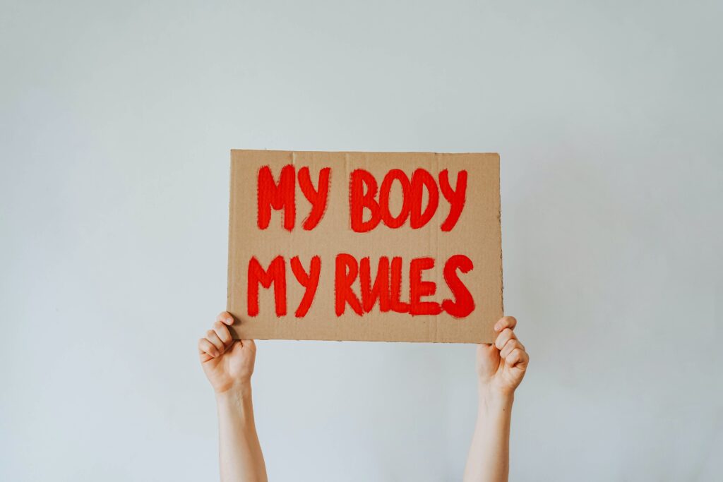 A woman's hands hold up a cardboard sign with "My body my rules" painted on it in red.