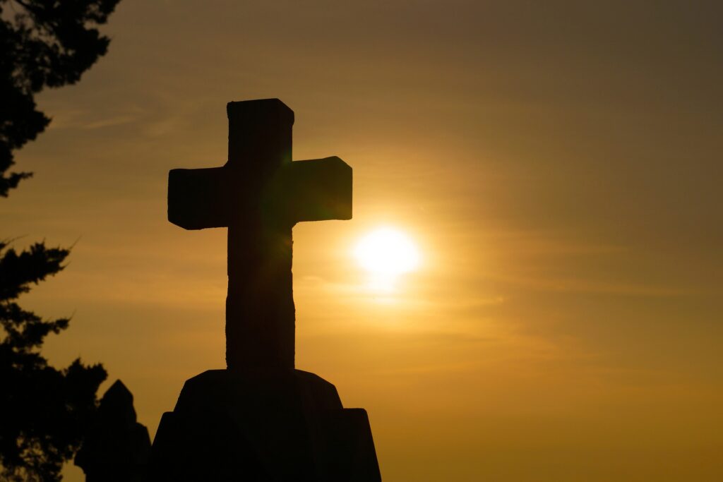 The silhouette of an old stone cross is shown with the backdrop of an orange sunset.