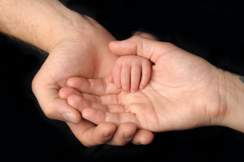 Two Caucasian adult hands, one in the other, with a baby's hand in them.