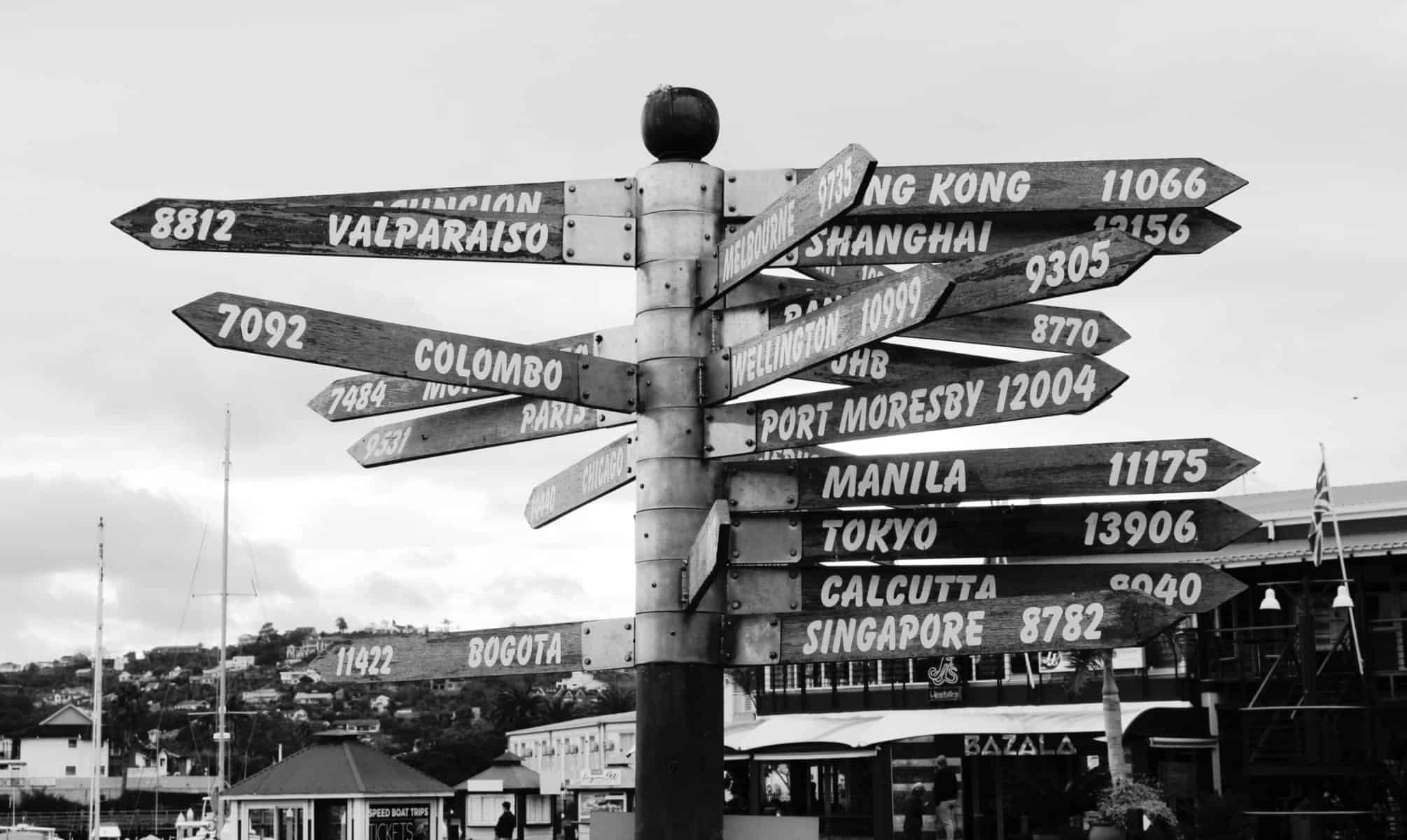 a pole stands with many signs stating how far to various global locations in black and white