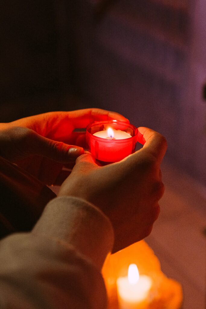 A pair of hands holds a small red votive with candle lit.