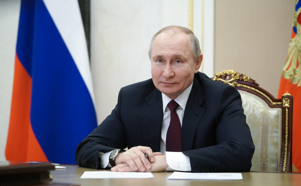 photo of Putin sitting at a desk with a Russian flag to the side