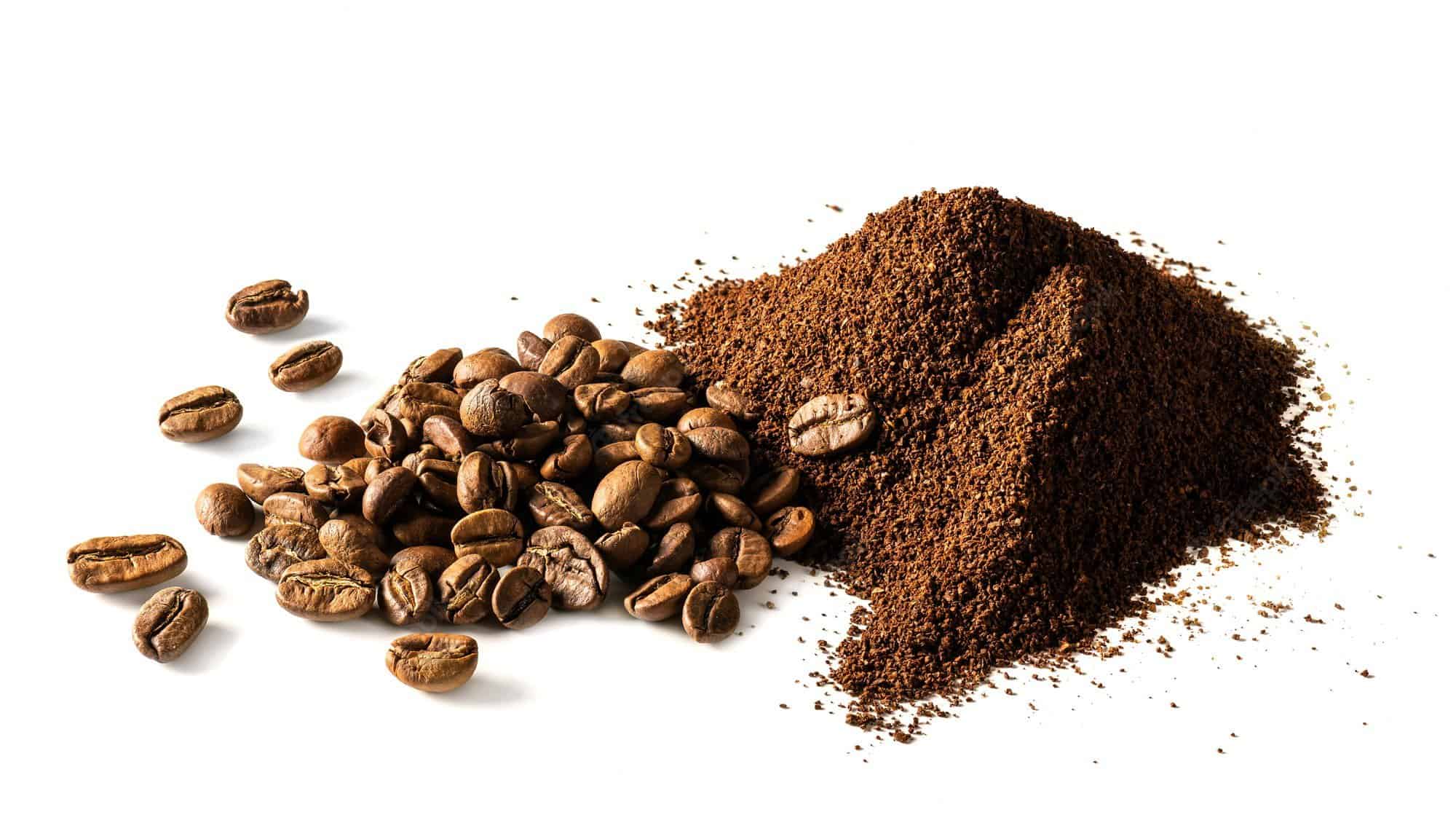 coffee beans and a pile of grounds sit on a white surface lit with a soft light
