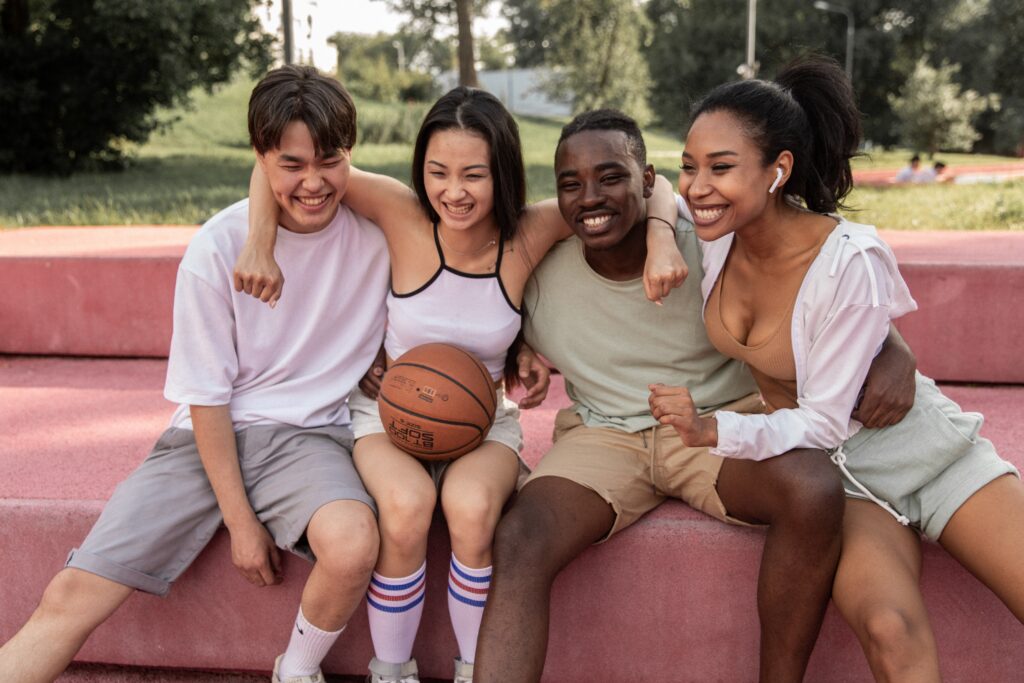a group of four non-caucasian teens, two boys, two girls, sits on a bench laughing and smiling