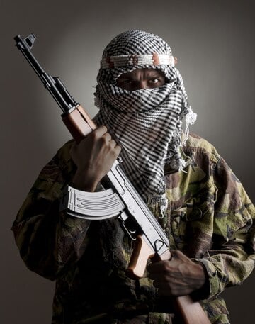 man with a covered face and dark skin holding a long gun in front of him