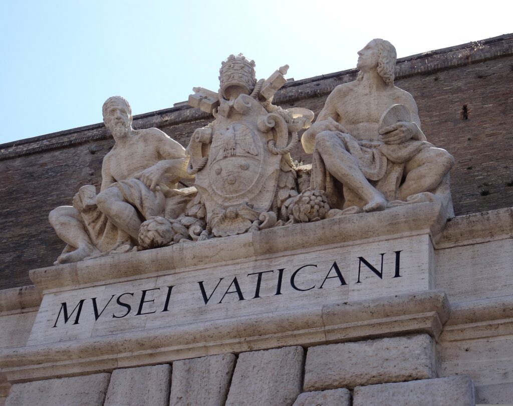 The stone lintel is inscribed with a sign saying Vatican Museum with two very old stone statues of men above