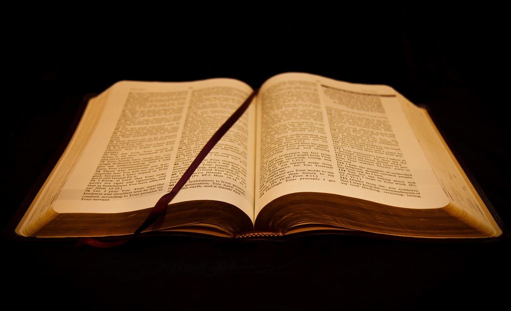 a bible as seen from the bottom sits laying open in the middle with the end of a red bookmark drawn to the center of the left page