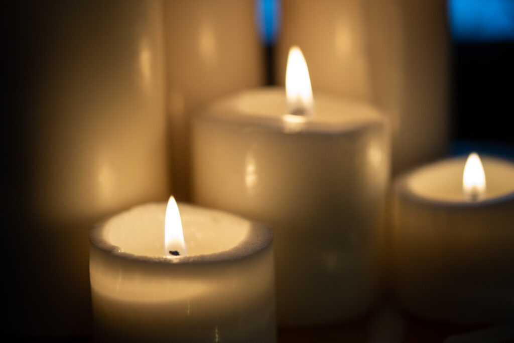 close up photo of off white and lit pillar candles of various heights are clustered together
