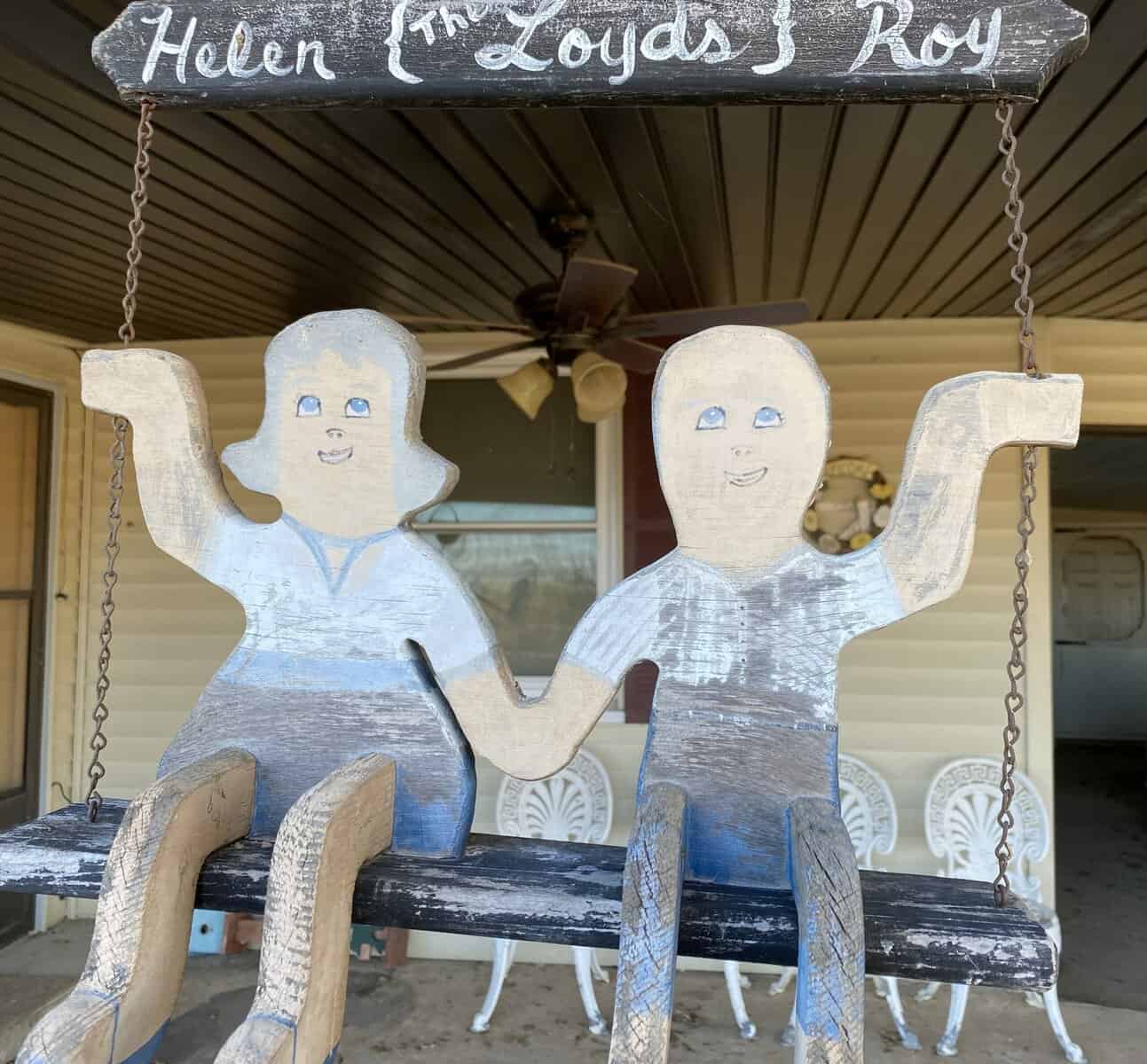 male and female wood cut outs sit on a wooden 'bench' holding hands with a sign above saying Helen and Roy, the Loyd's