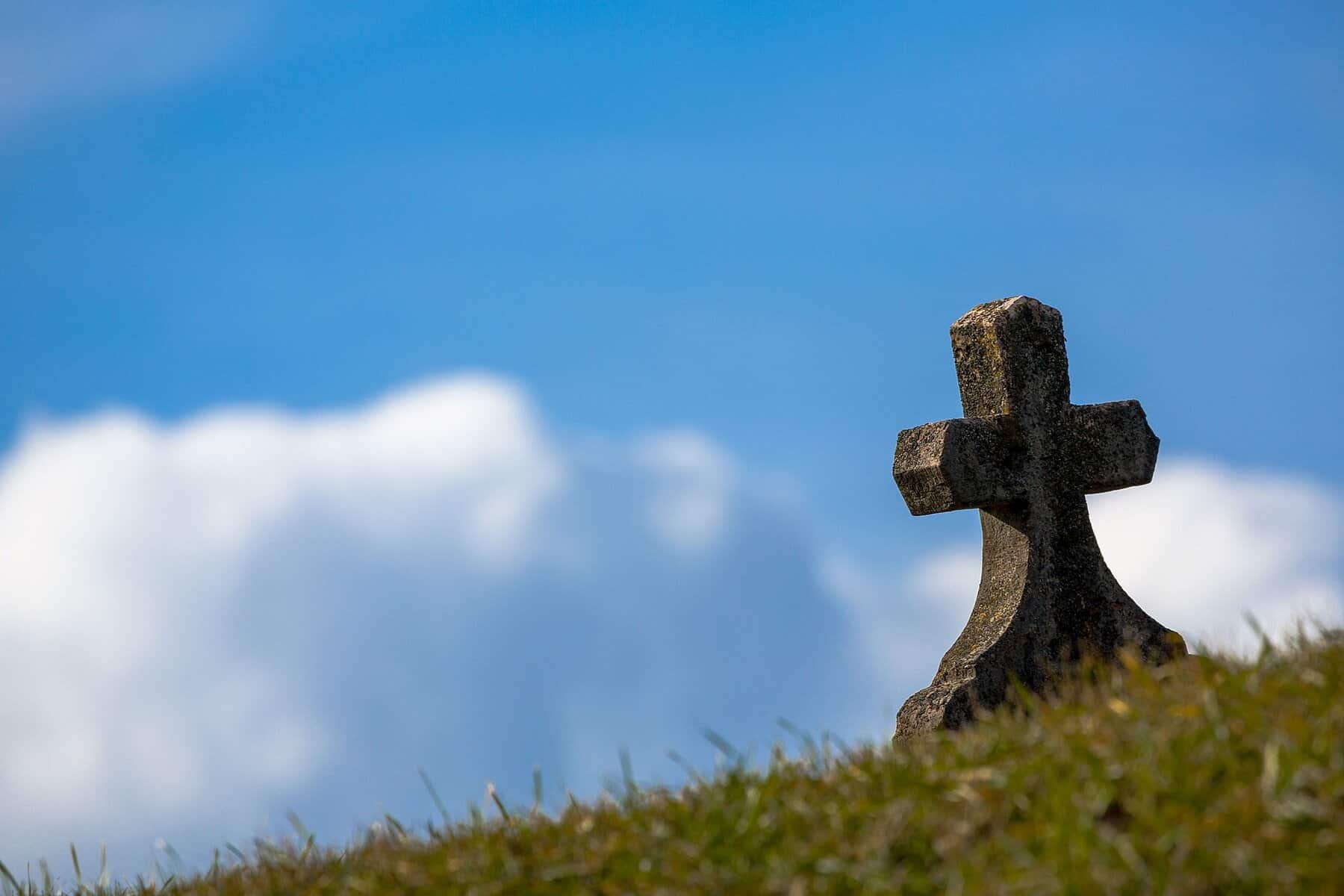 small very old stone cross at the top of a grave stone as seen from the back