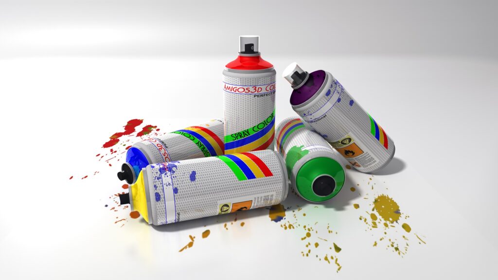 Five cans or various colored spray paint are standing and laying together in a white background with paint splatters
