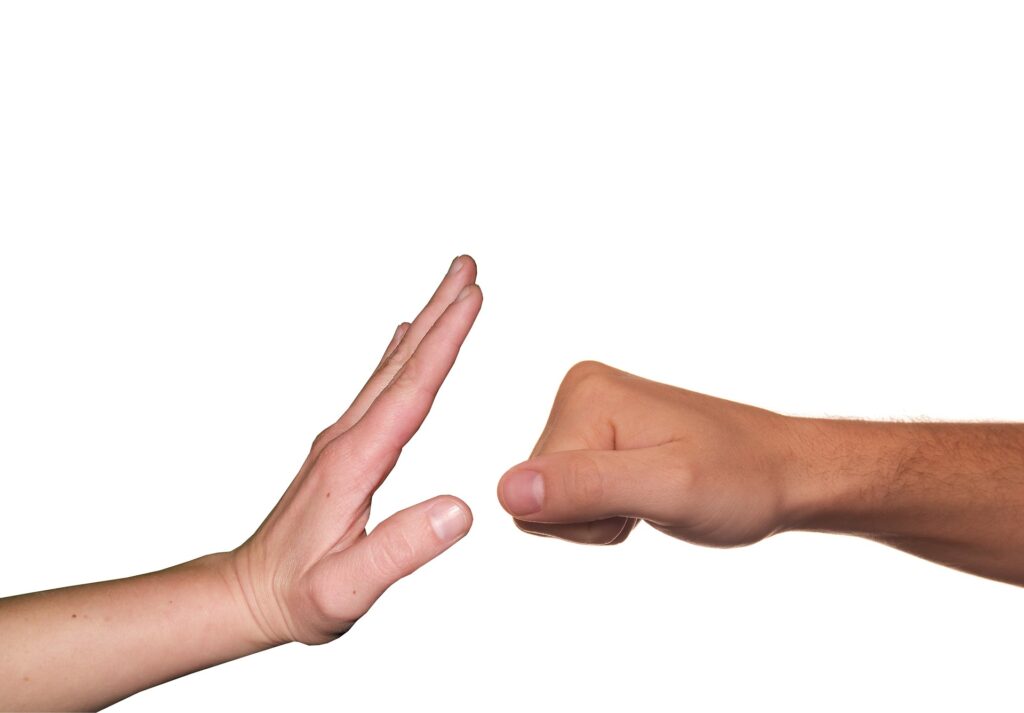 two hands are against a white backdrop. One hand is open facing a hand made into a fist as if to block the fist