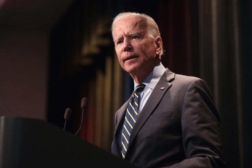 President Joe Biden is shown in a dark grey suit and speaking at an event.