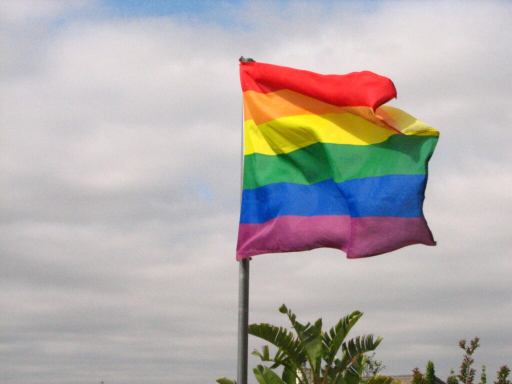 A Pride flag is seen waving in the wind atop a flagpole.
