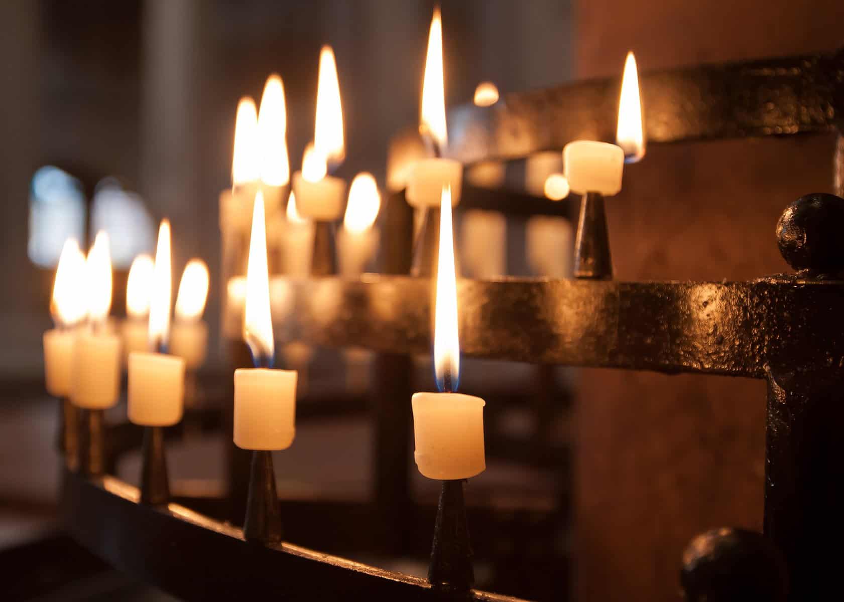 Lit white pillar candles on an iron holder as if on an altar.
