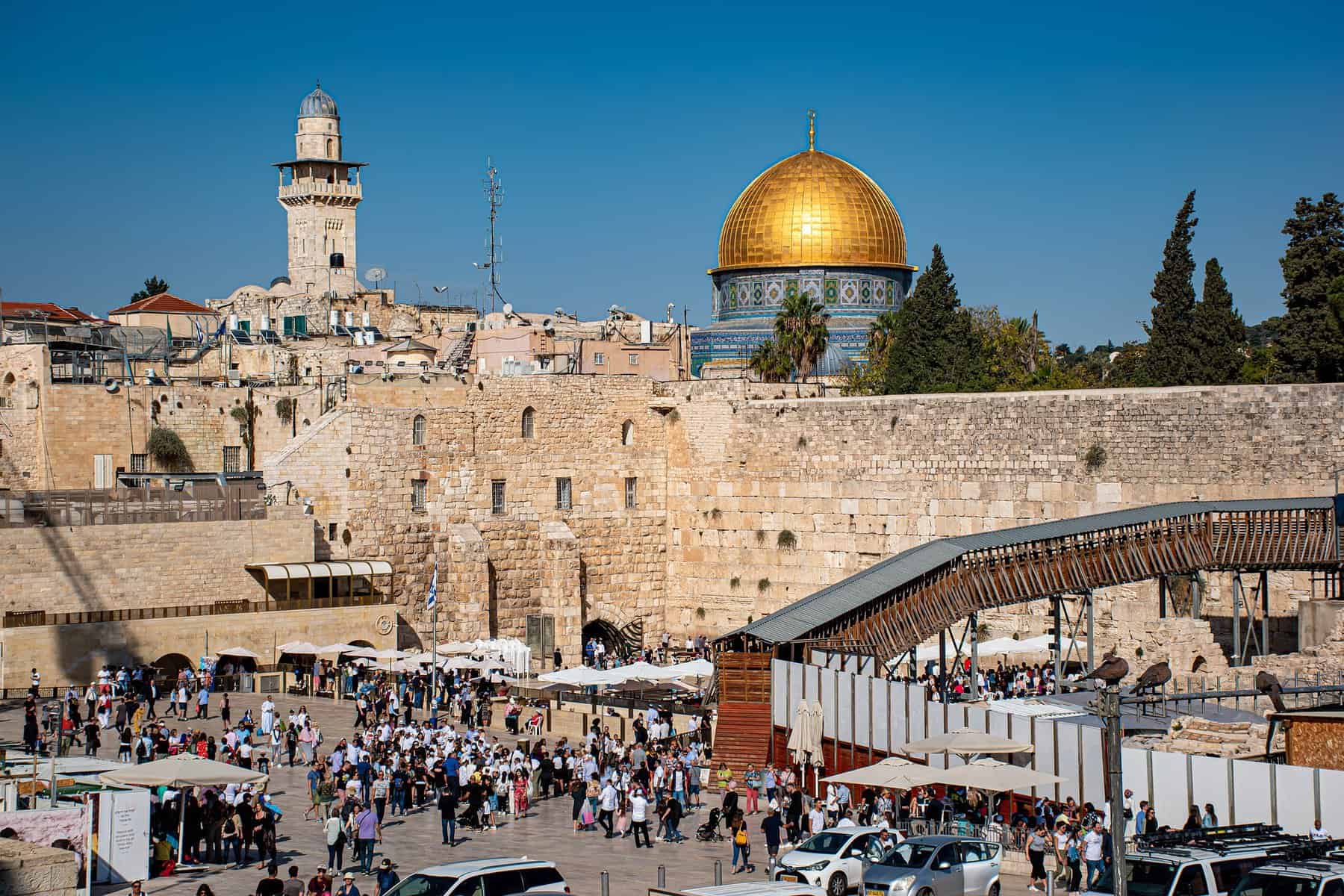 Image shows a street view of Jerusalem with the Dome of the Rock in the distance.