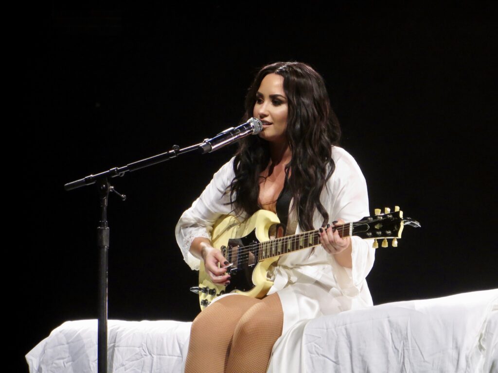 Demi Lovato is shown sitting and playing a guitar.