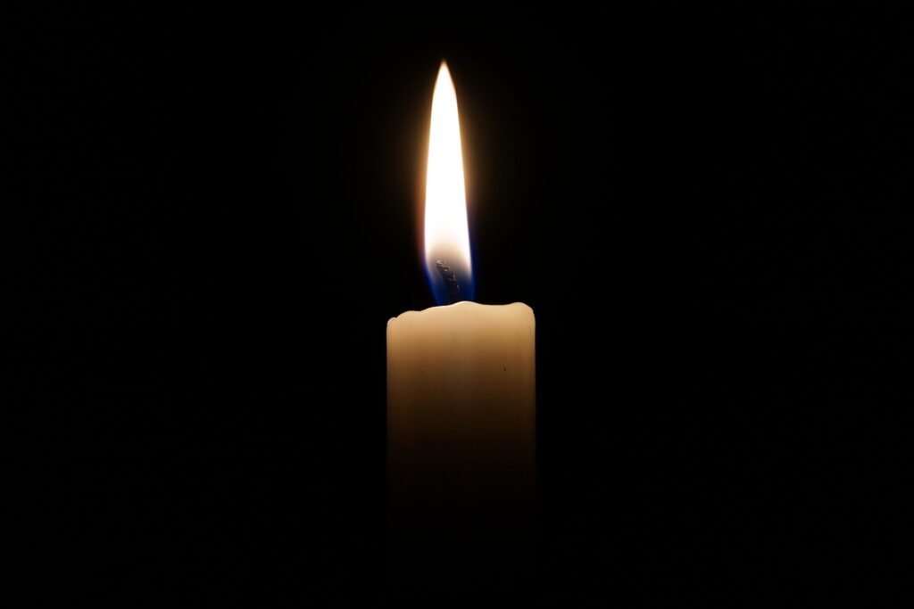 A lone white candle is shown lit while surrounded by darkness.