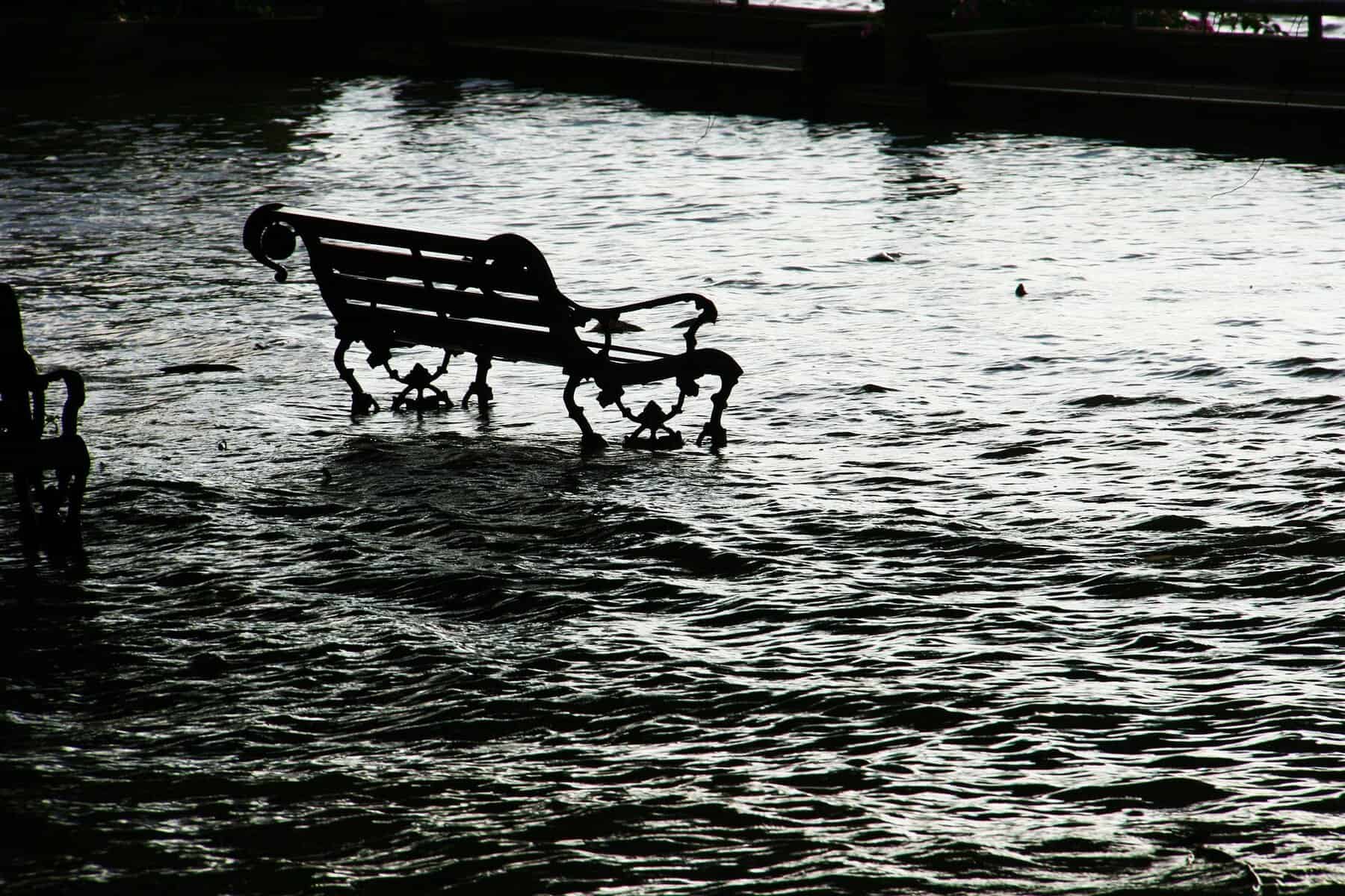 A bench sits surrounded by floodwaters in this black and white image.