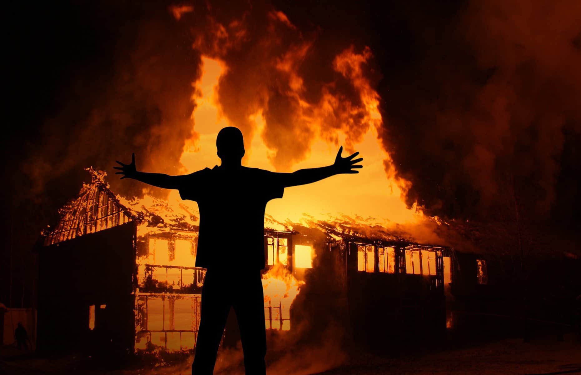 The silhouette of a person is shown in front of a blazing bonfire at night.