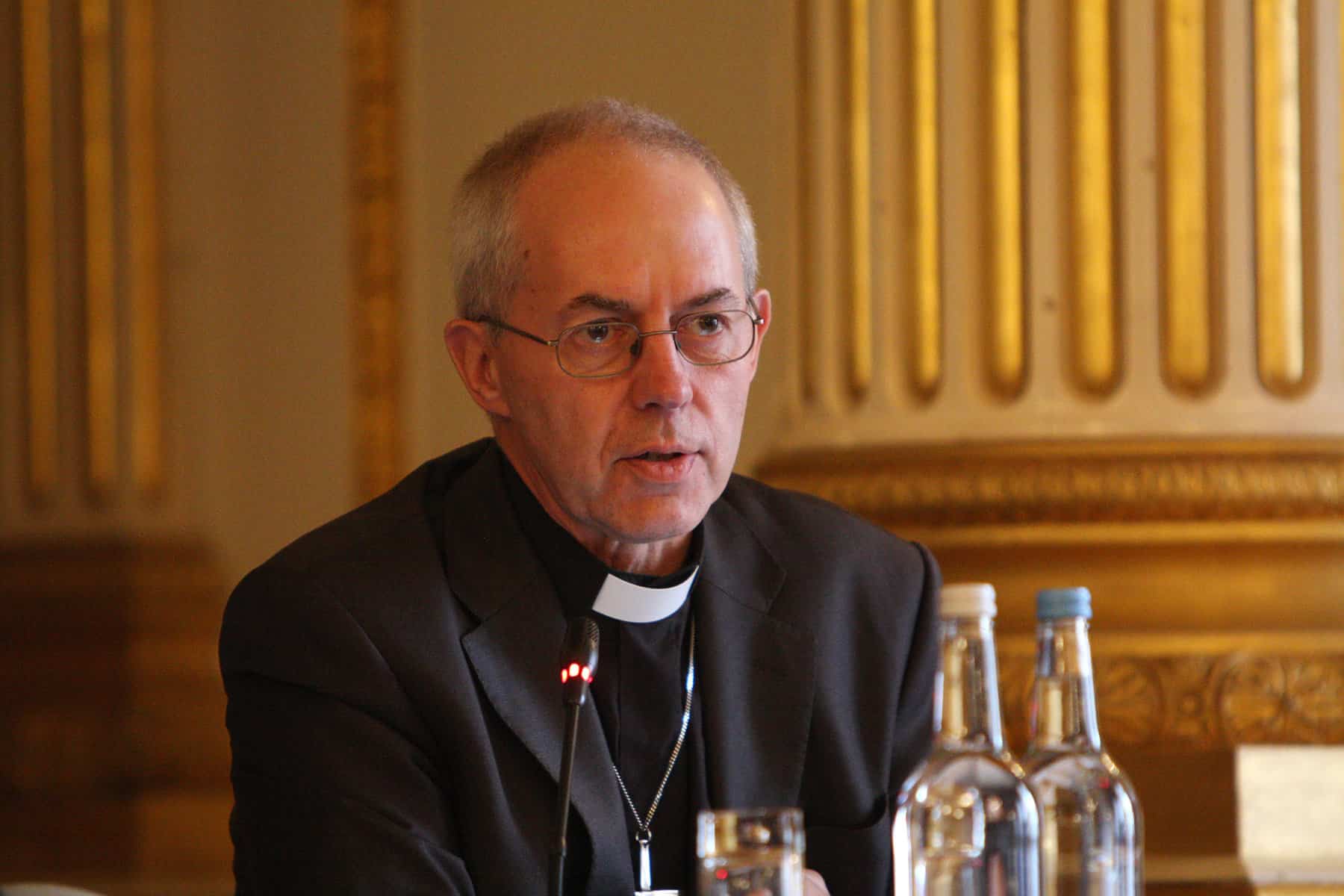 Justin Welby is shown seated at a table and speaking.