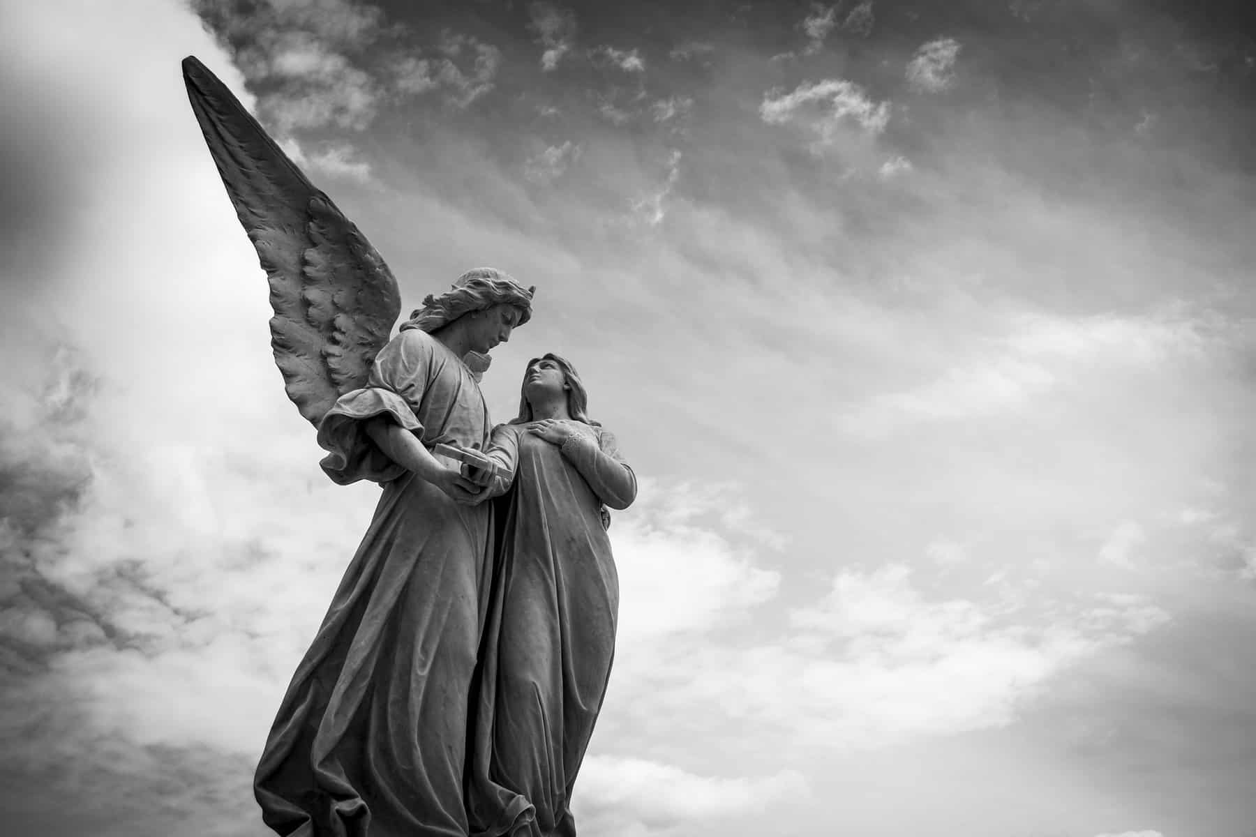 This black and white image shows the statue of an angel appearing to protect a person.