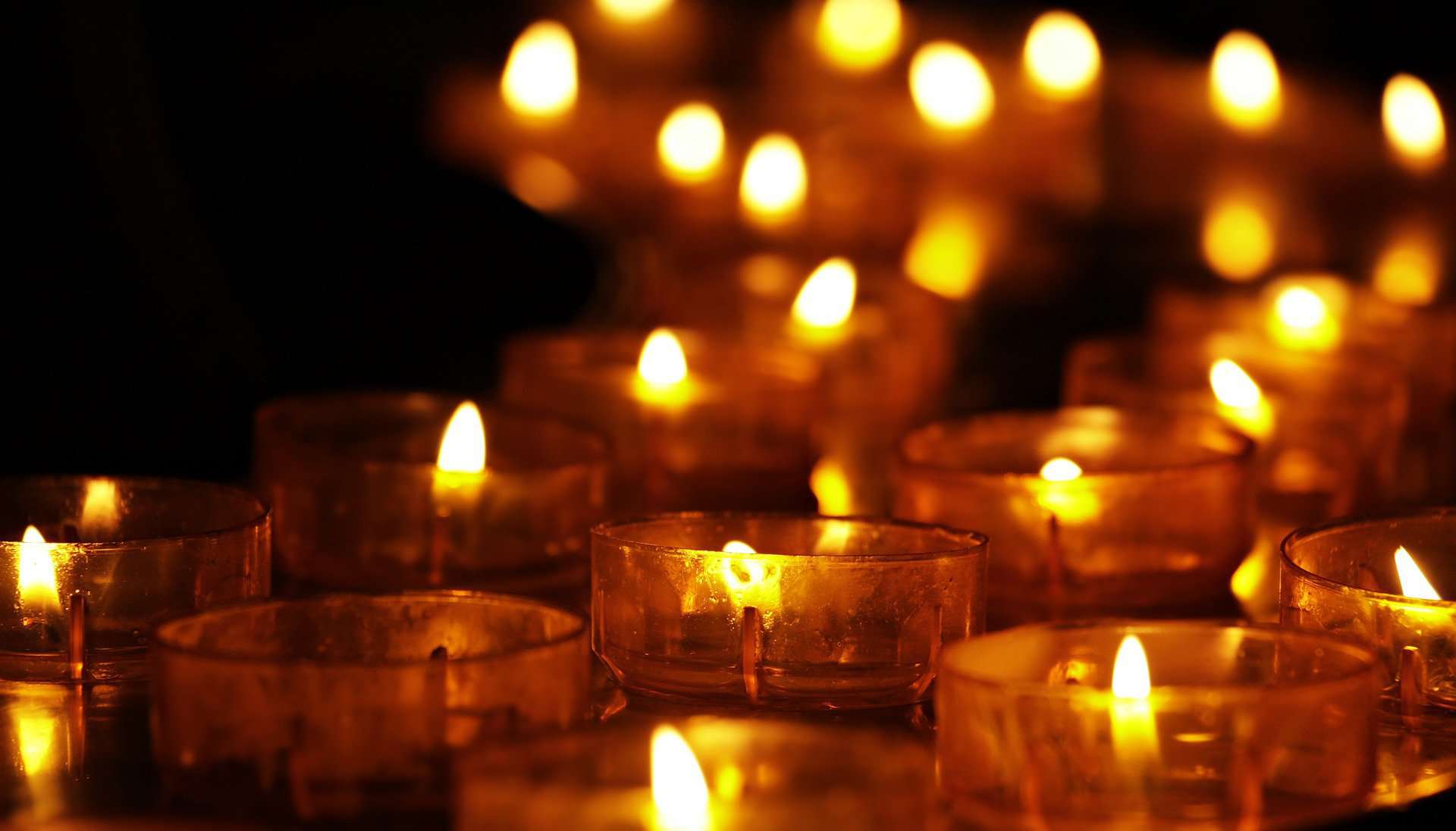 A large group of candles in amber glass are lit in a dark space.