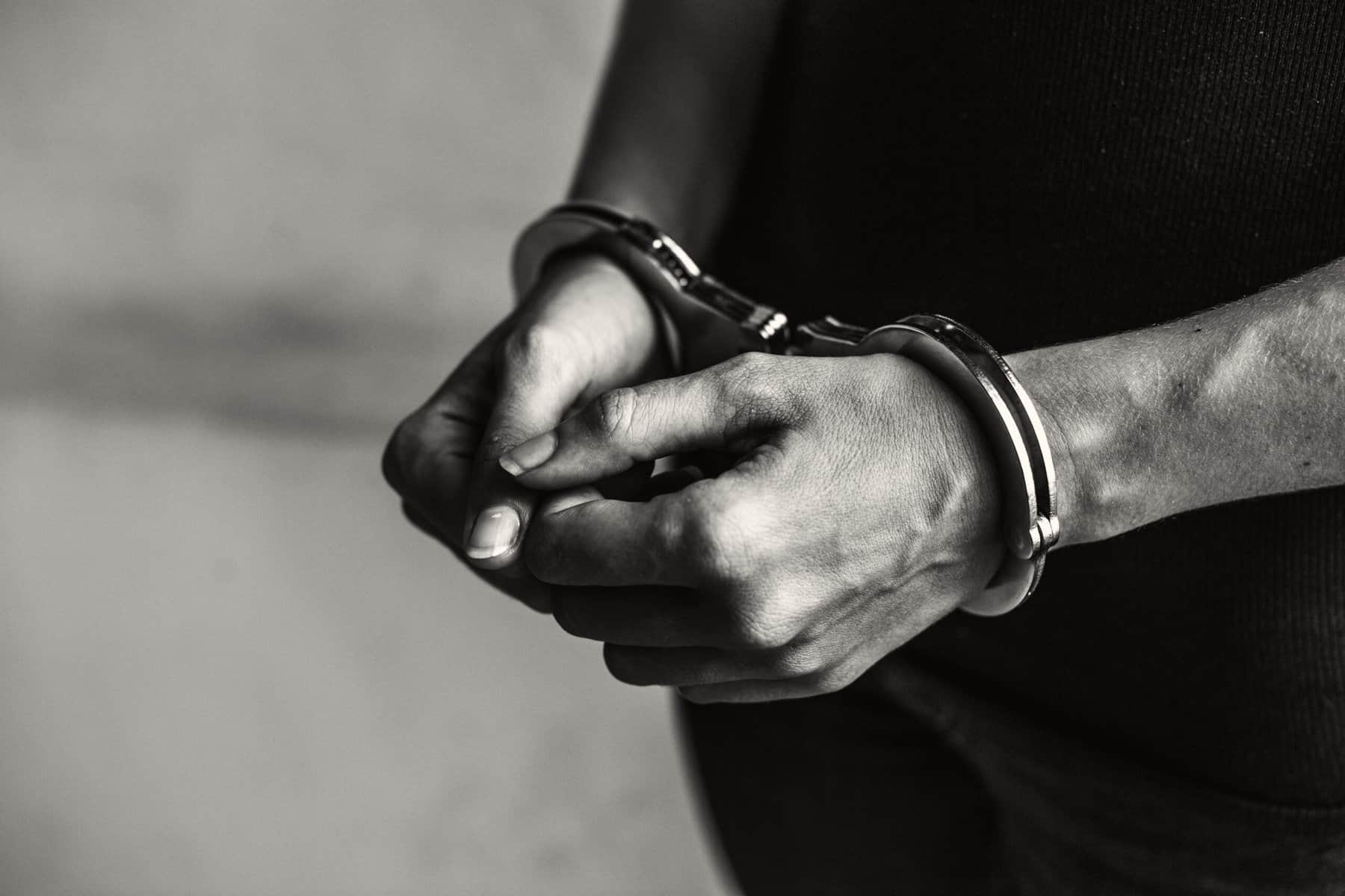 A prisoner's forearms and hands are shown with handcuffs on the wrists in this black and white image.