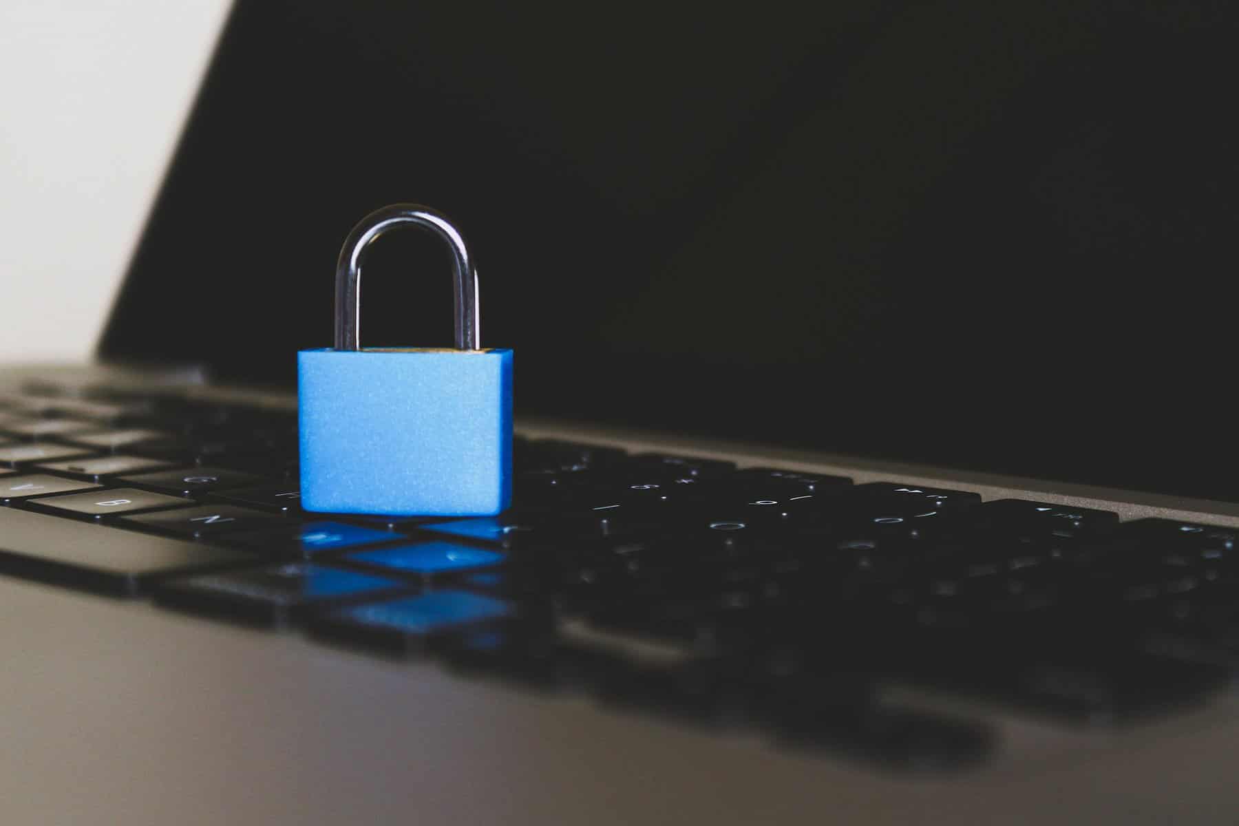 A blue padlock is shown sitting on the keyboard of a laptop.
