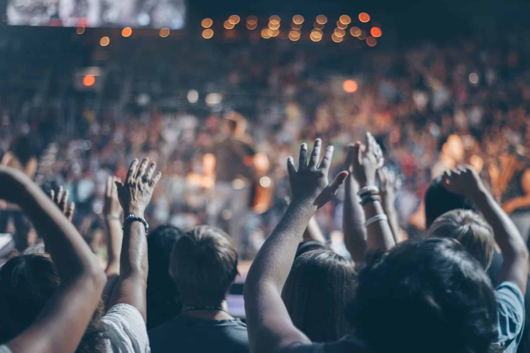 Hands of a crowd are raised in a concert like venue with dramatic lighting.