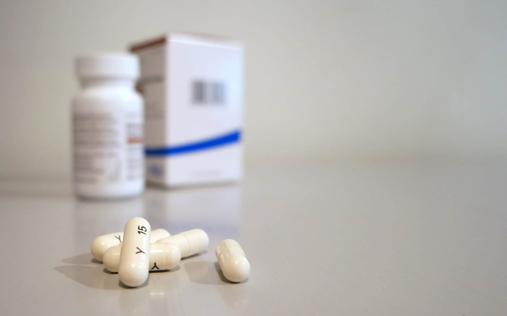 Prescription medicine capsules are shown with the Rx bottle and box in the background.
