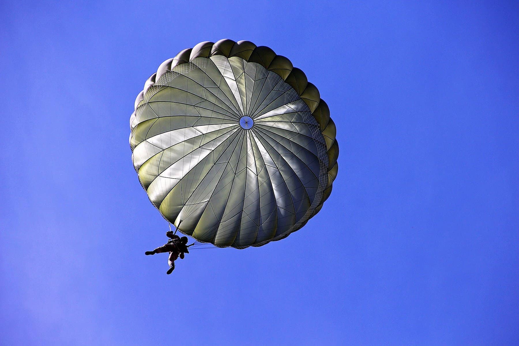 A person is shown from below dangling from a white, fully expended parachute.