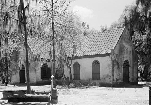 An older, small light colored church is shown in this black and white image.
