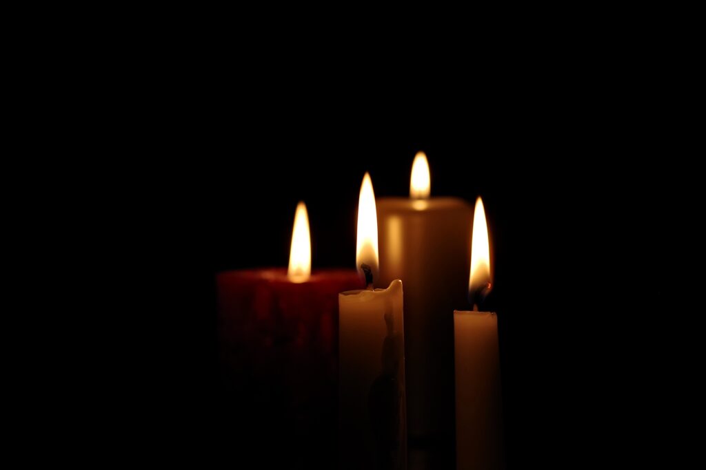 Four lit candles are in a dark space.