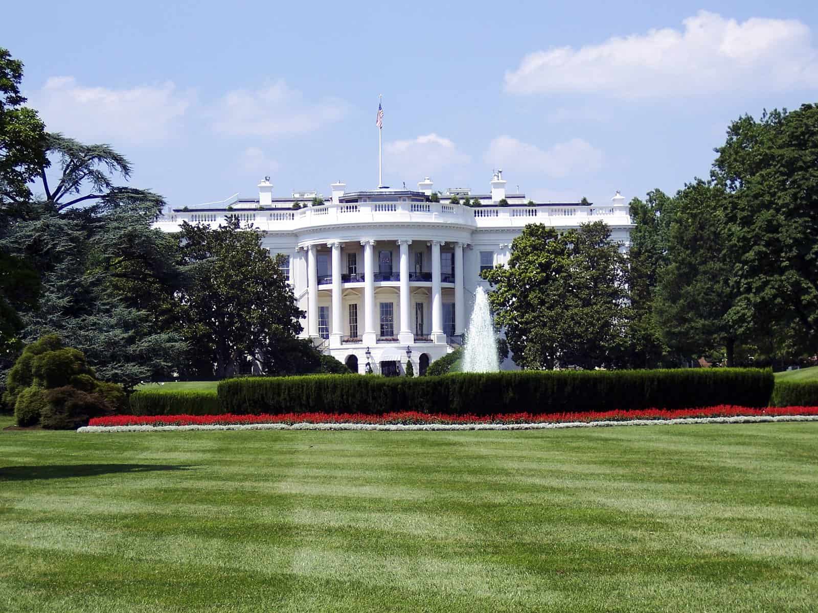 The White House is shown at a distance across a green lawn.