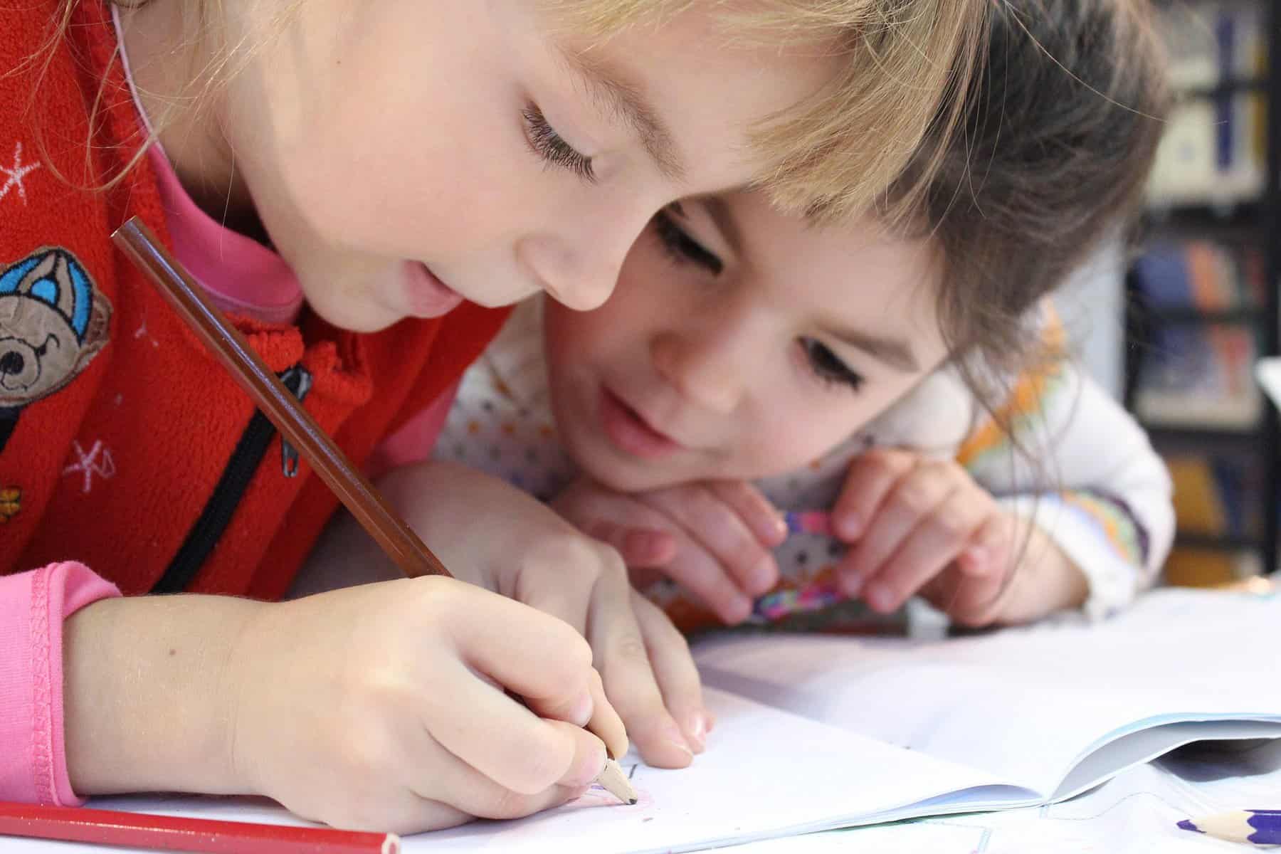 Two children are shown close up and working on writing something.