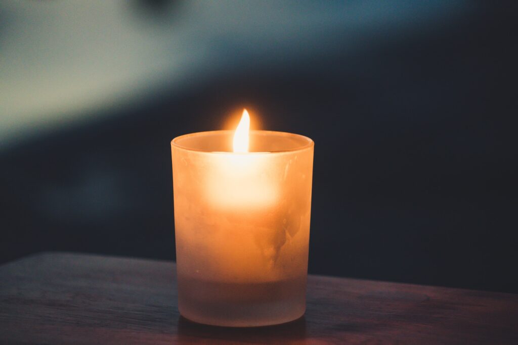 A small candle votive is shown lit in a semi-dark environment.