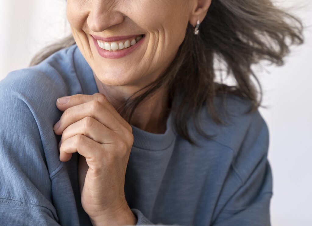 A woman is shown from under the eyes down to clavicle wearing a blue sweatshirt and smiling.