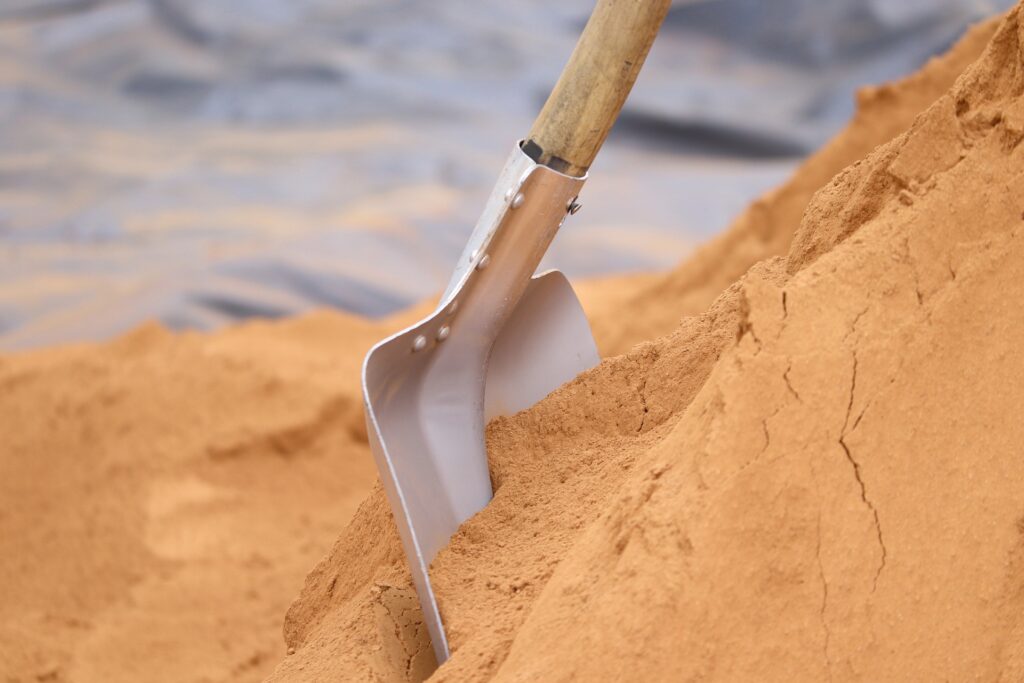 A shovel is shown stuck in a pile of golden dirt, perhaps sand.